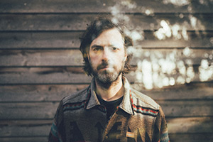 Foto des Solokünstlers Gregor MCEwan vor einer Holzwand